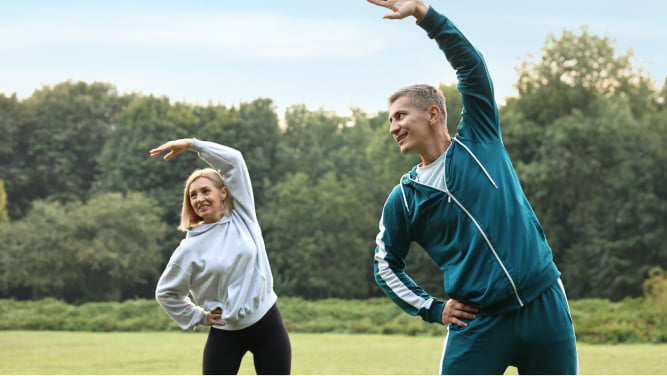 A man and a woman stretching their arms in the forest