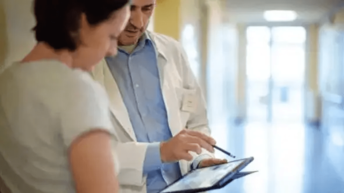 A doctor using a stylus to show information on a tablet to a patient