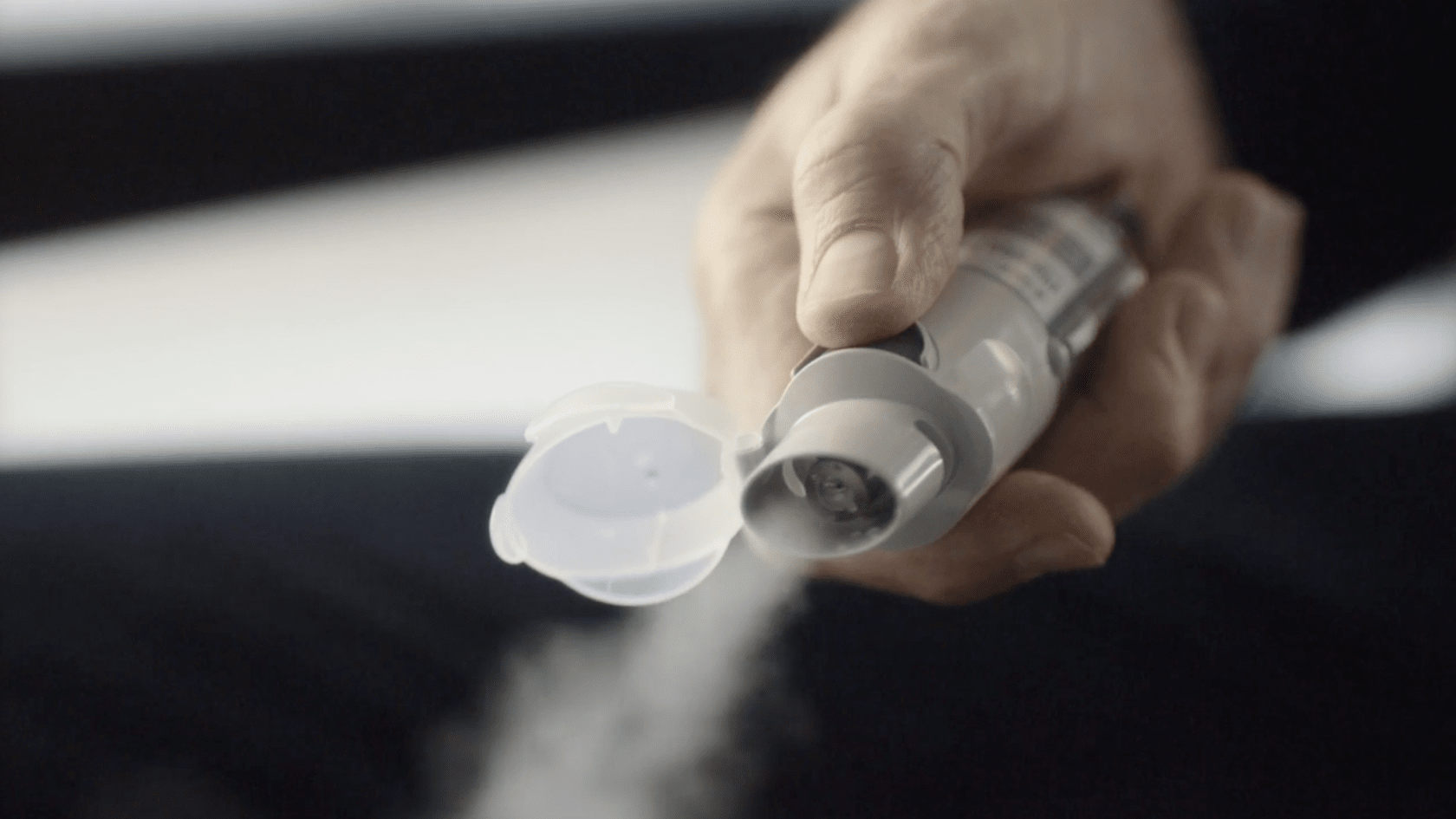 Hand holding the Spiriva Respimat inhaler pointed downward while releasing a mist spray