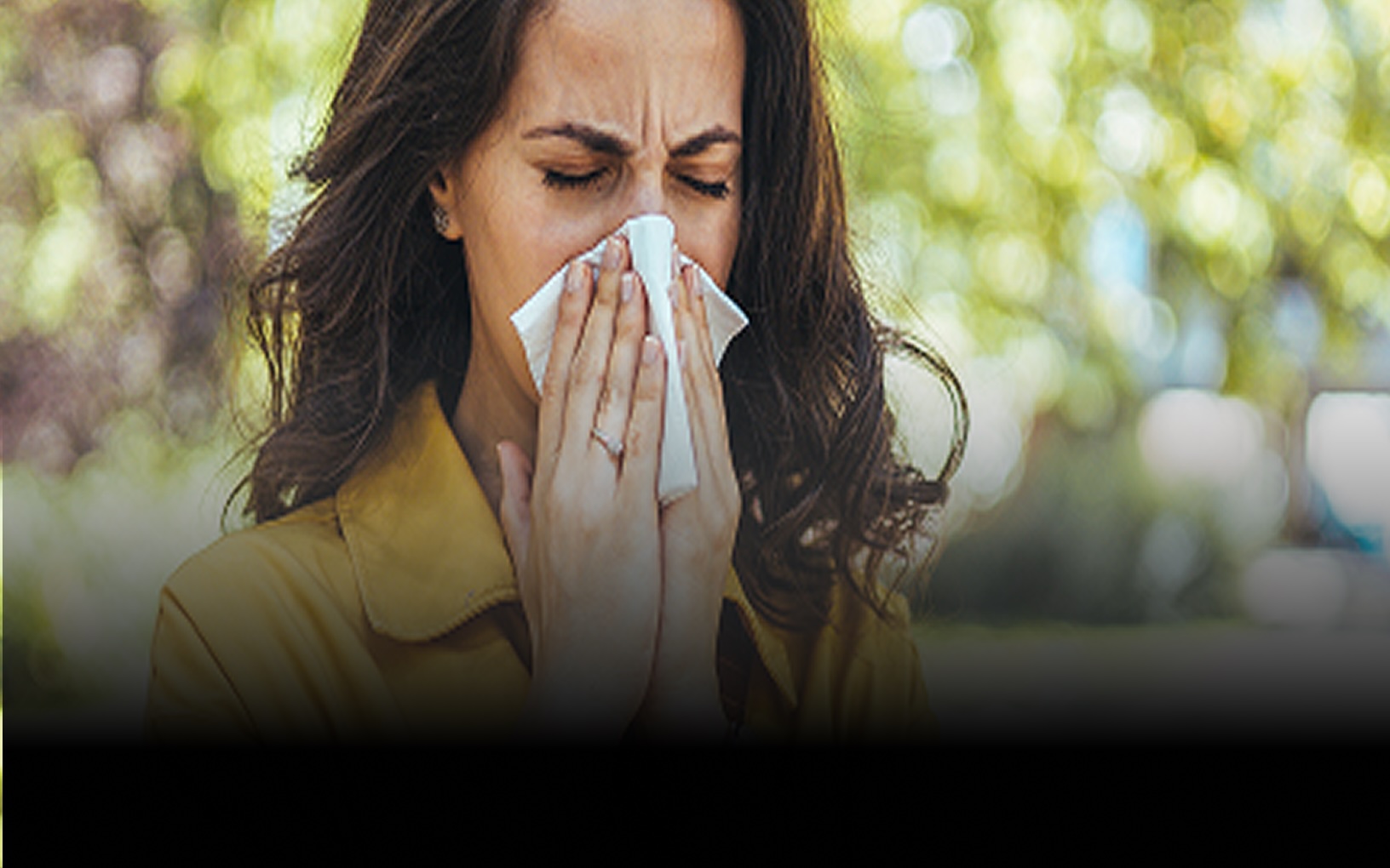 Woman in yellow jacket blowing her nose with a tissue outdoors